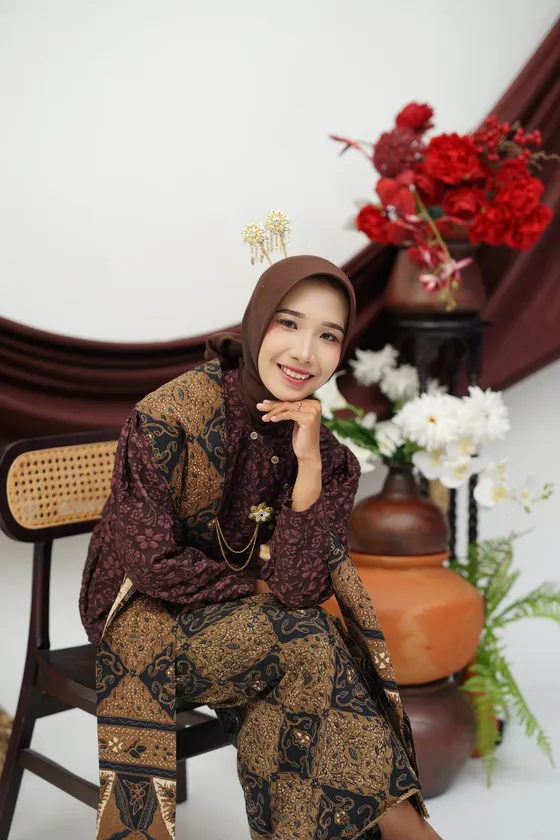 Mempelai wanita dalam kebaya cokelat dan kain batik, duduk tersenyum