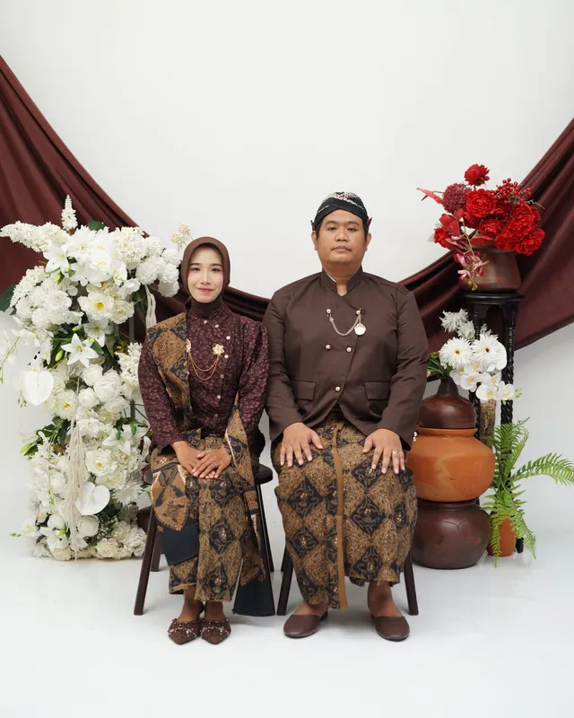 Kedua mempelai duduk berdampingan di kursi rotan