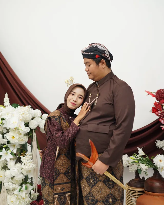 Kedua mempelai berpose berdekatan di antara bunga putih