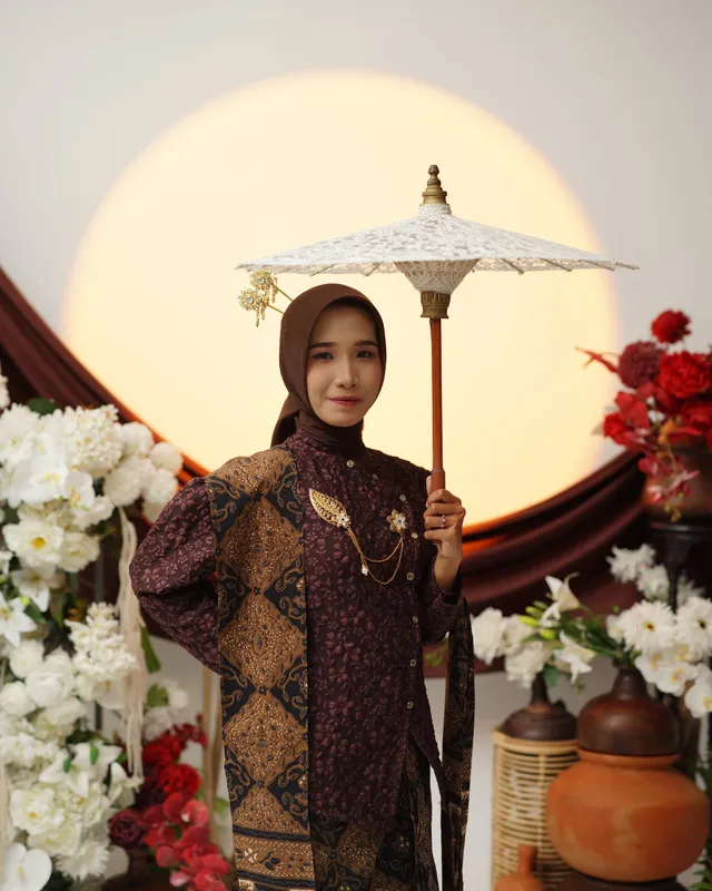 Mempelai wanita berdiri membawa payung putih di depan latar cahaya